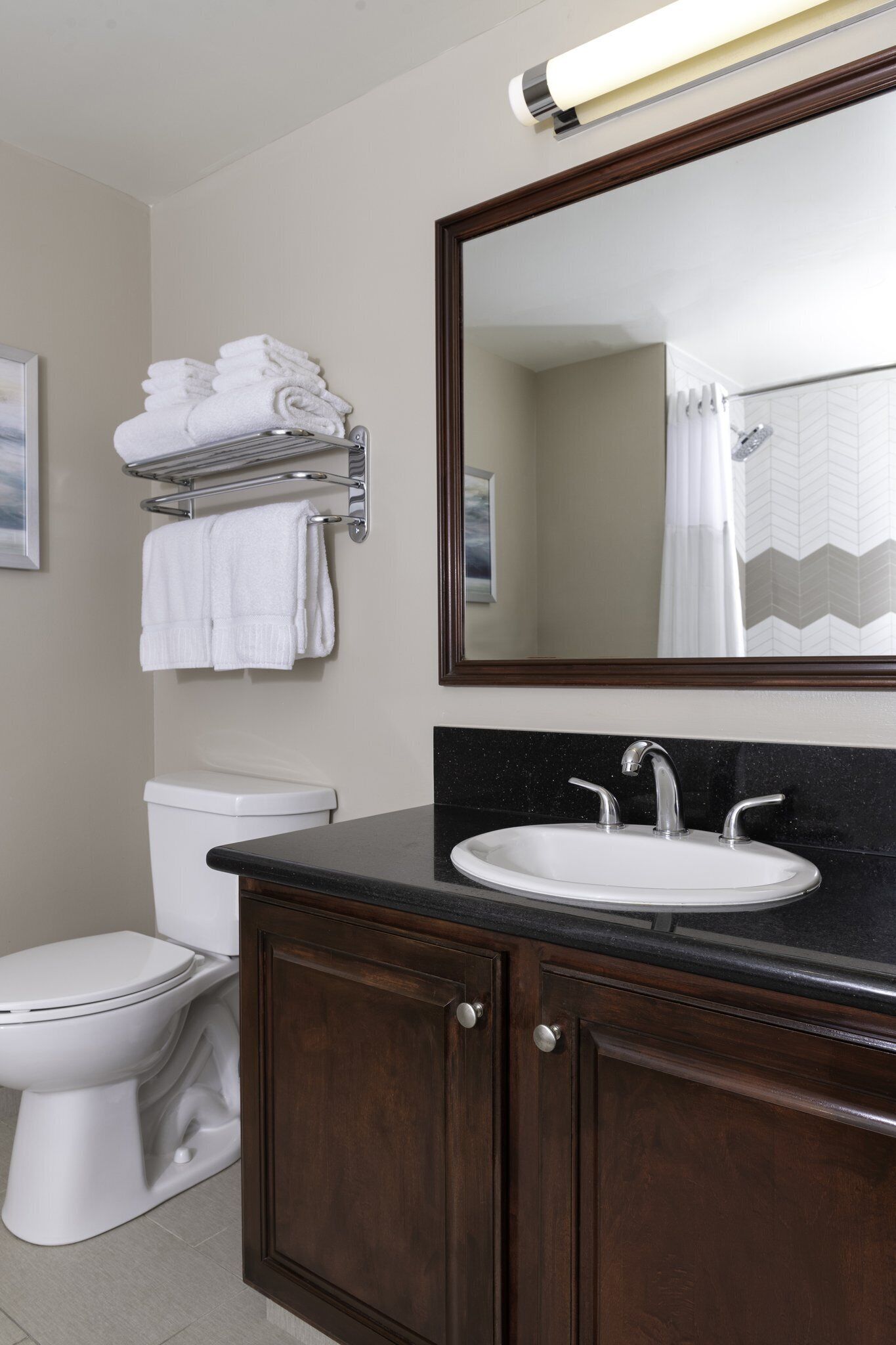 Une salle de bain avec des toilettes blanches, un lavabo surmonté d’un miroir et un porte-serviettes avec des serviettes pliées.