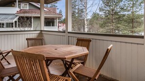 A covered patio with a wooden table and chairs, overlooking a residential area with houses and trees. - Mustikka by Interhome (Sotkamo)