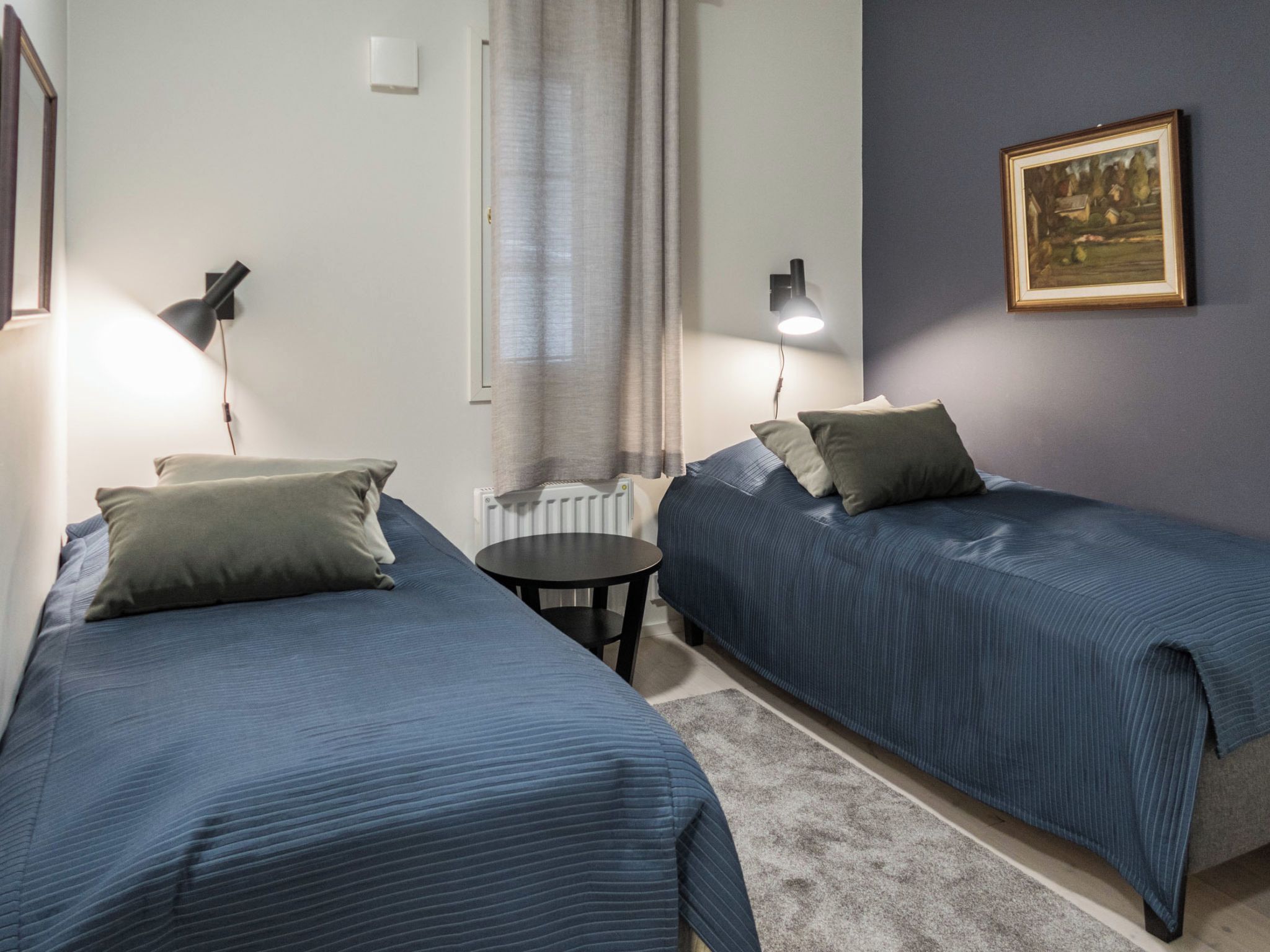 Una habitación con dos camas, una mesita y un cuadro en la pared.