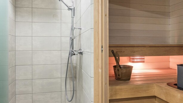 A modern bathroom with a shower, wooden bench, and a small kitchen area with a bucket and utensils. - Mustikka by Interhome (Sotkamo)