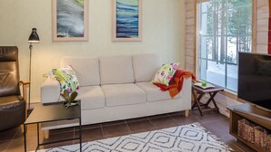 Una sala de estar con un sofá, una mesa de centro, un mueble para televisión y dos cuadros en la pared.