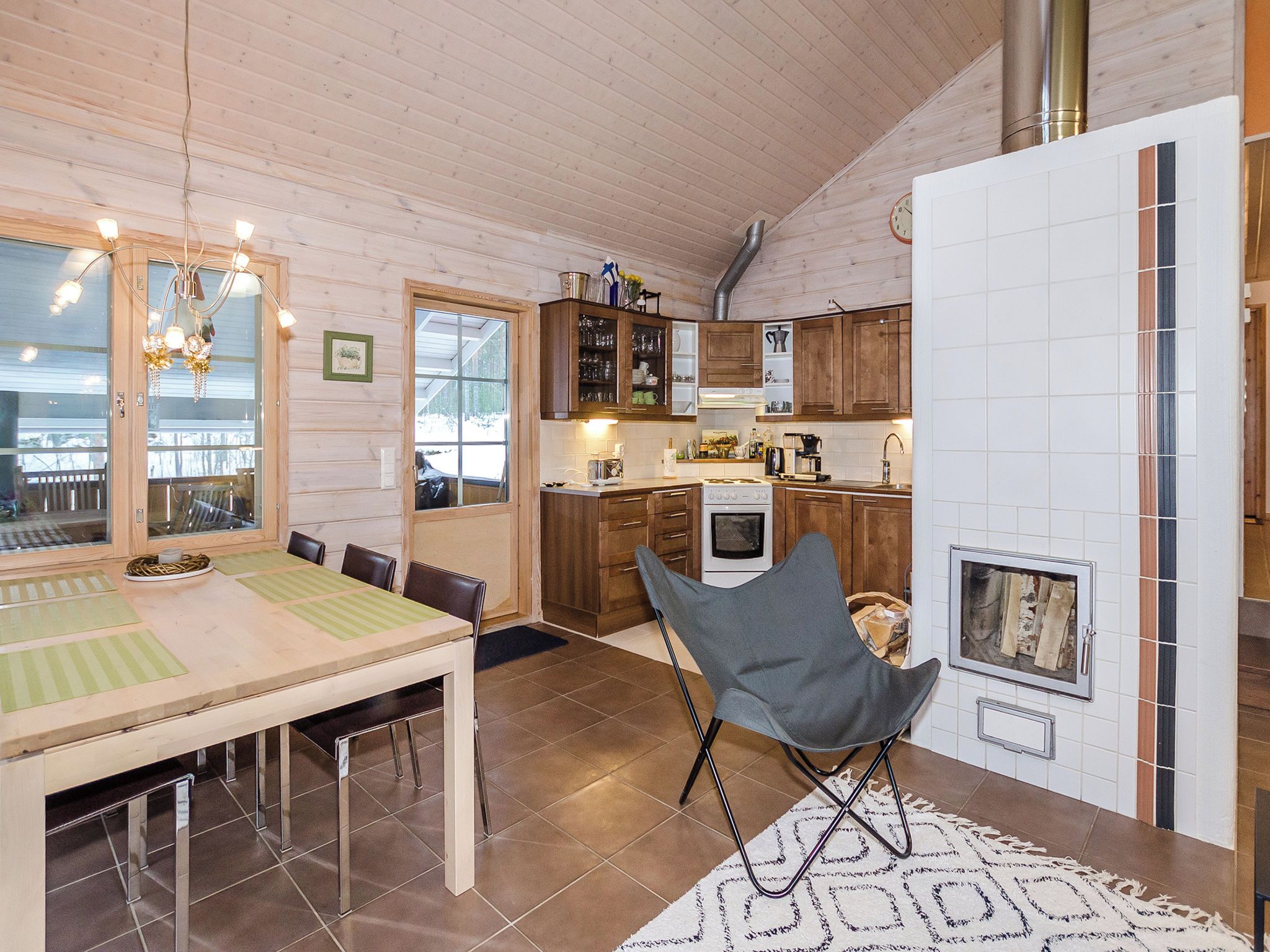 A cozy kitchen with wooden cabinets, a dining table with chairs, a fireplace, and a view through a window.