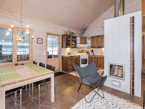 A cozy kitchen with wooden cabinets, a dining table with chairs, a fireplace, and a view through a window.
