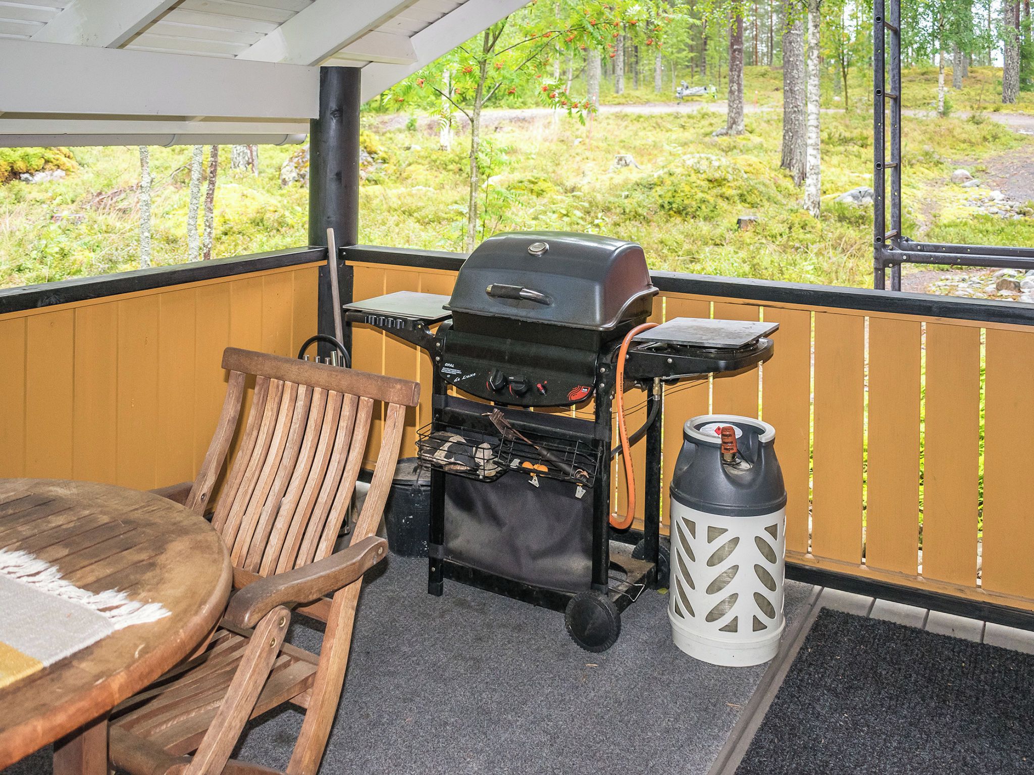 Eine Holzterrasse mit Grill, Stuhl und Laterne.