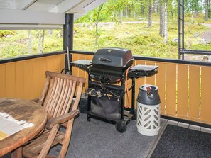 Una terraza de madera con una parrilla, una silla y un farol.