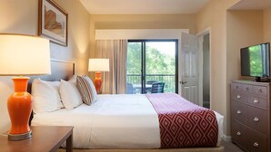 Una habitación de hotel con una cama, dos lámparas de noche, un aparador, un televisor y vistas al exterior a través de una puerta corrediza.