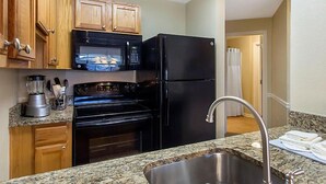 Una cocina con armarios de madera, un refrigerador negro, un microondas, un horno y una encimera de granito.