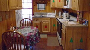 Une cuisine compacte avec des meubles en bois, une table à manger avec un set de table, un réfrigérateur, un four à micro-ondes et une cuisinière.