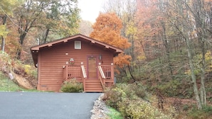 Une petite cabane à un seul étage, dotée d’un porche à l’avant, et entourée d’arbres aux couleurs automnales.