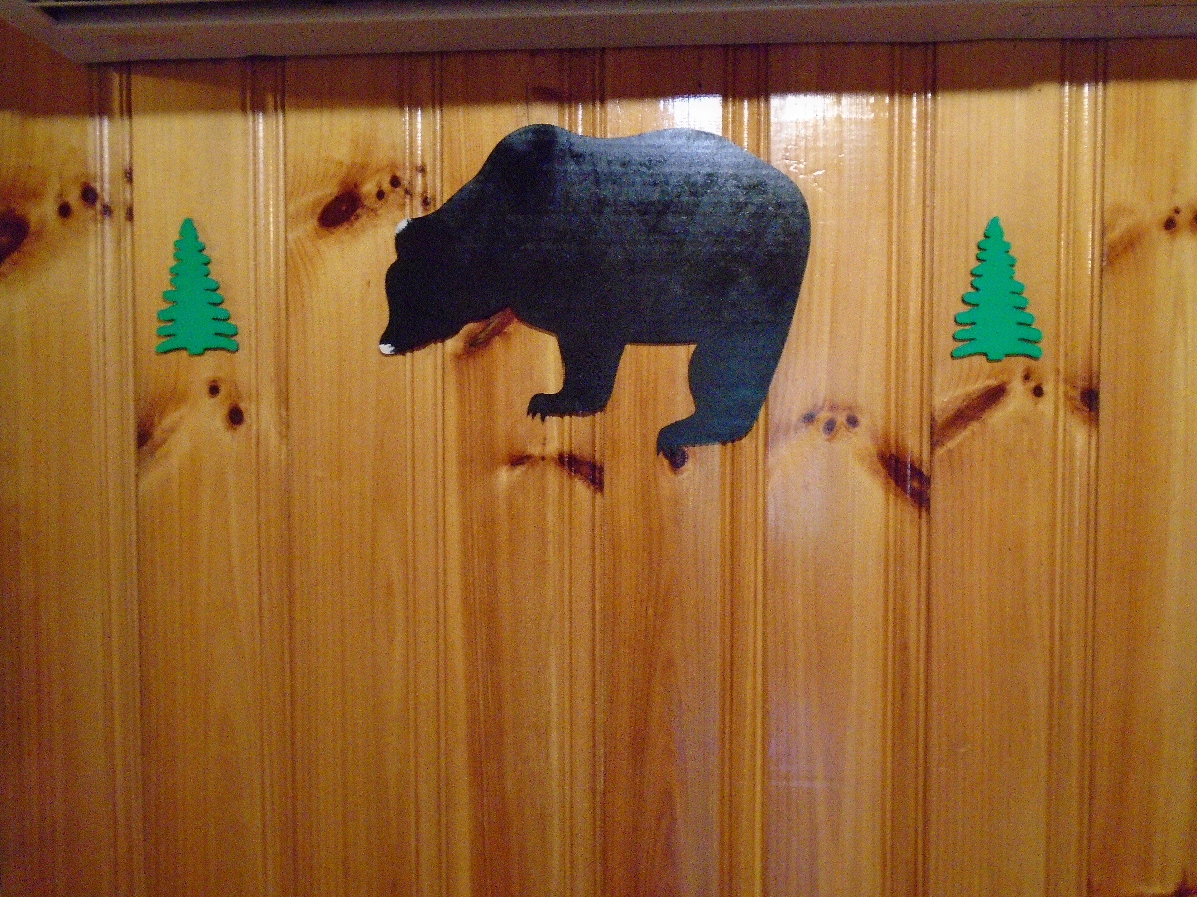 A wooden wall with a bear silhouette and two green tree cutouts.
