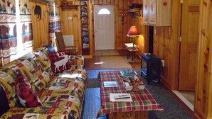 L’intérieur d’un chalet accueillant, avec un canapé, une table sur laquelle sont disposés divers objets, une lampe et des murs en bois.