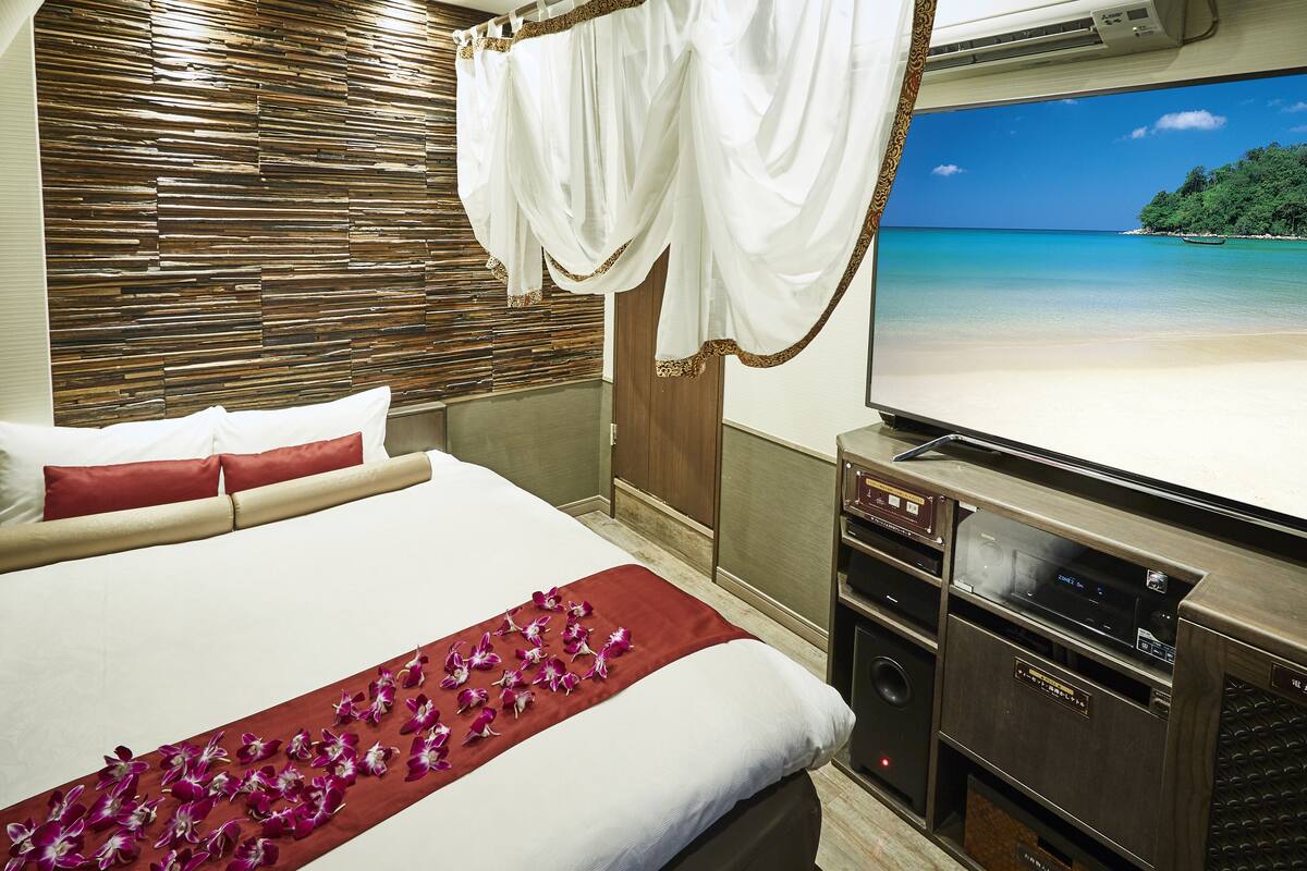 A hotel room with a bed, a television, and a view of a beach.