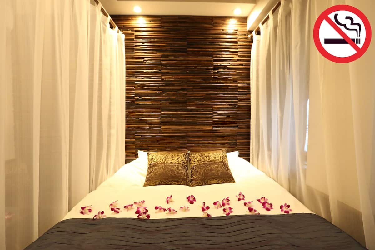 A hotel room with a bed, curtains, a no-smoking sign, and a wooden headboard.