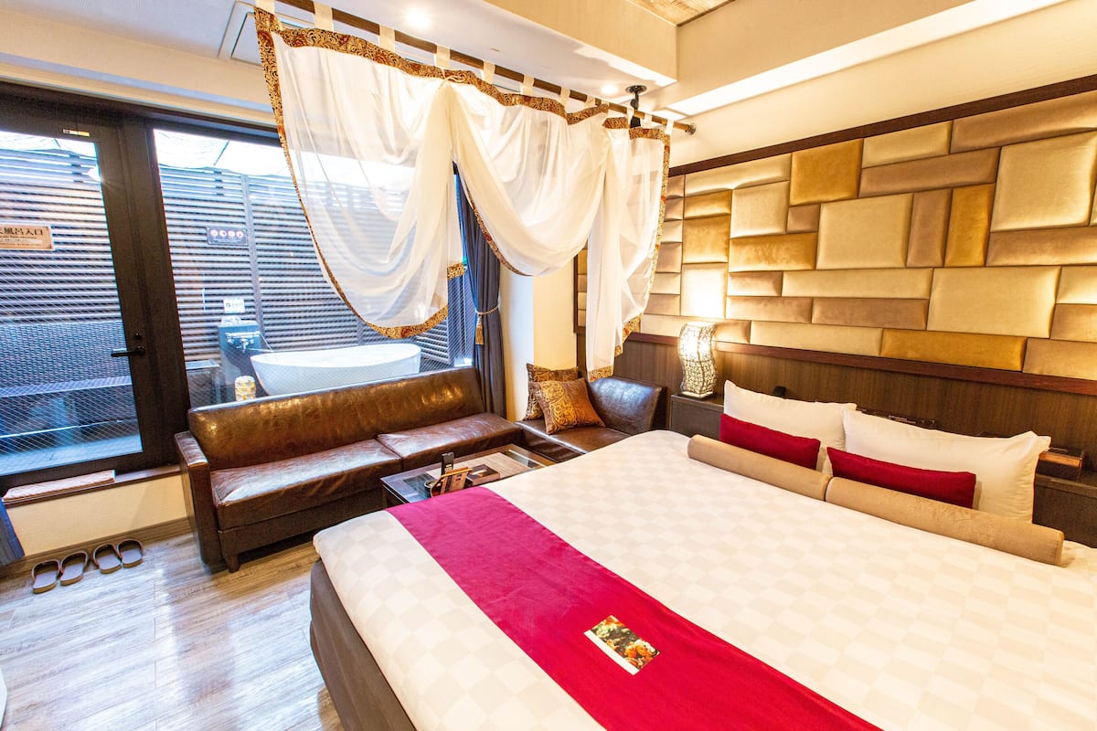 A hotel room with a large bed, a sofa, a small table, and a window with curtains.