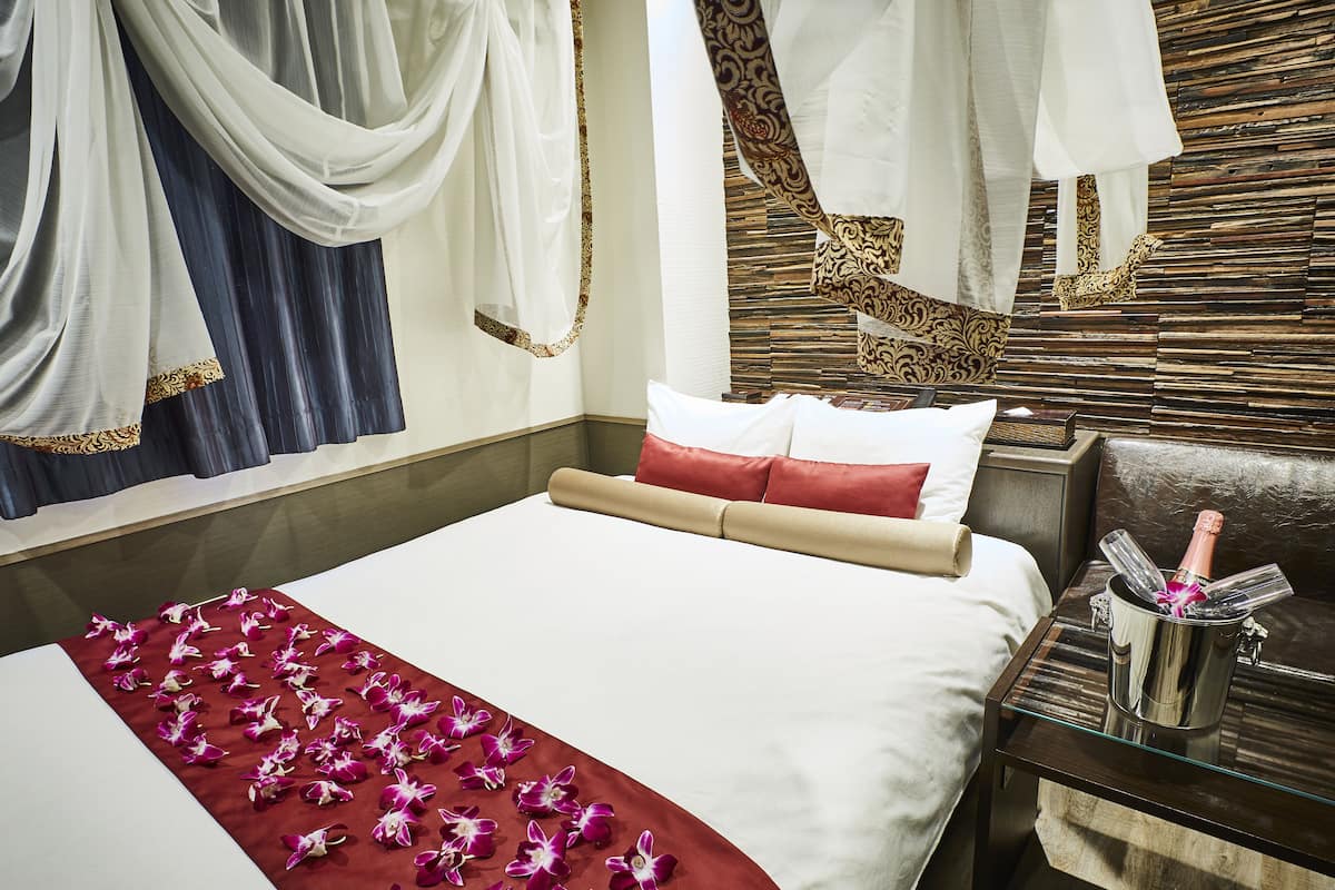 A hotel room with a bed, a nightstand with a bottle of champagne, and a decorative wall.