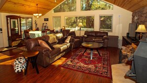 A spacious living room with a high ceiling, wooden floors, leather sofas, a coffee table, and a large window offering a view of the outdoors. - *Peaceful getaway *Close to Goldwater Lake *Cabin (Prescott)