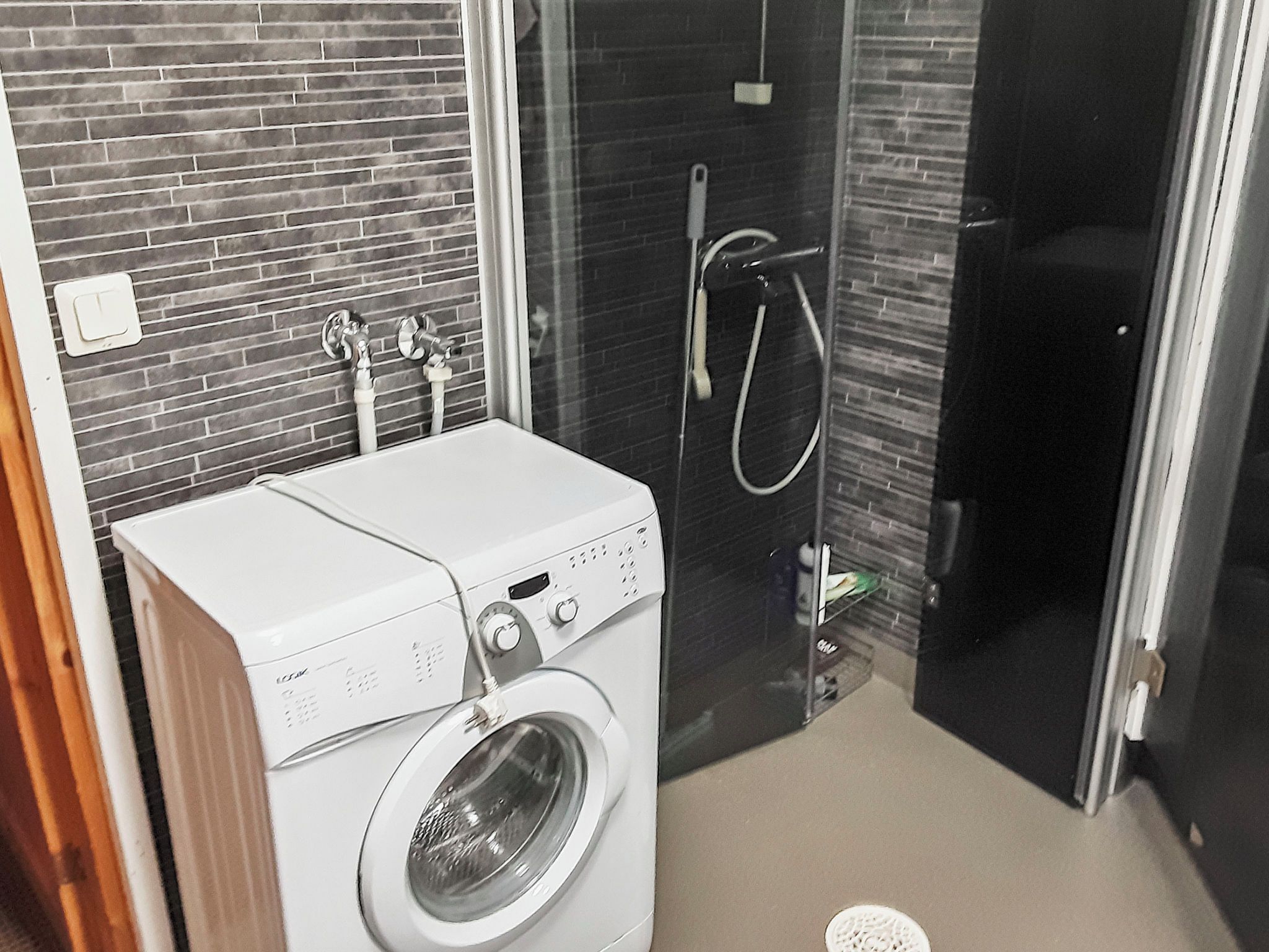 A compact laundry area with a front-loading washing machine and a glass-enclosed shower.