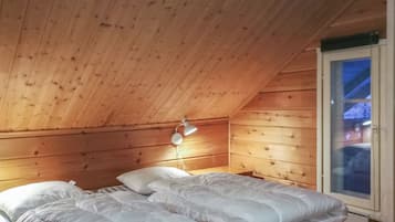 Ein Zimmer mit schrägen Wänden, Holzwänden, einem Bett mit weißer Bettwäsche und einer Nachttischlampe.