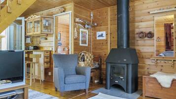 Interior acogedor de una cabaña con chimenea, paredes de madera, televisor y una zona de estar confortable.