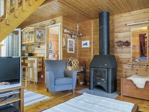 Interior acogedor de una cabaña con chimenea, paredes de madera, televisor y una zona de estar confortable.