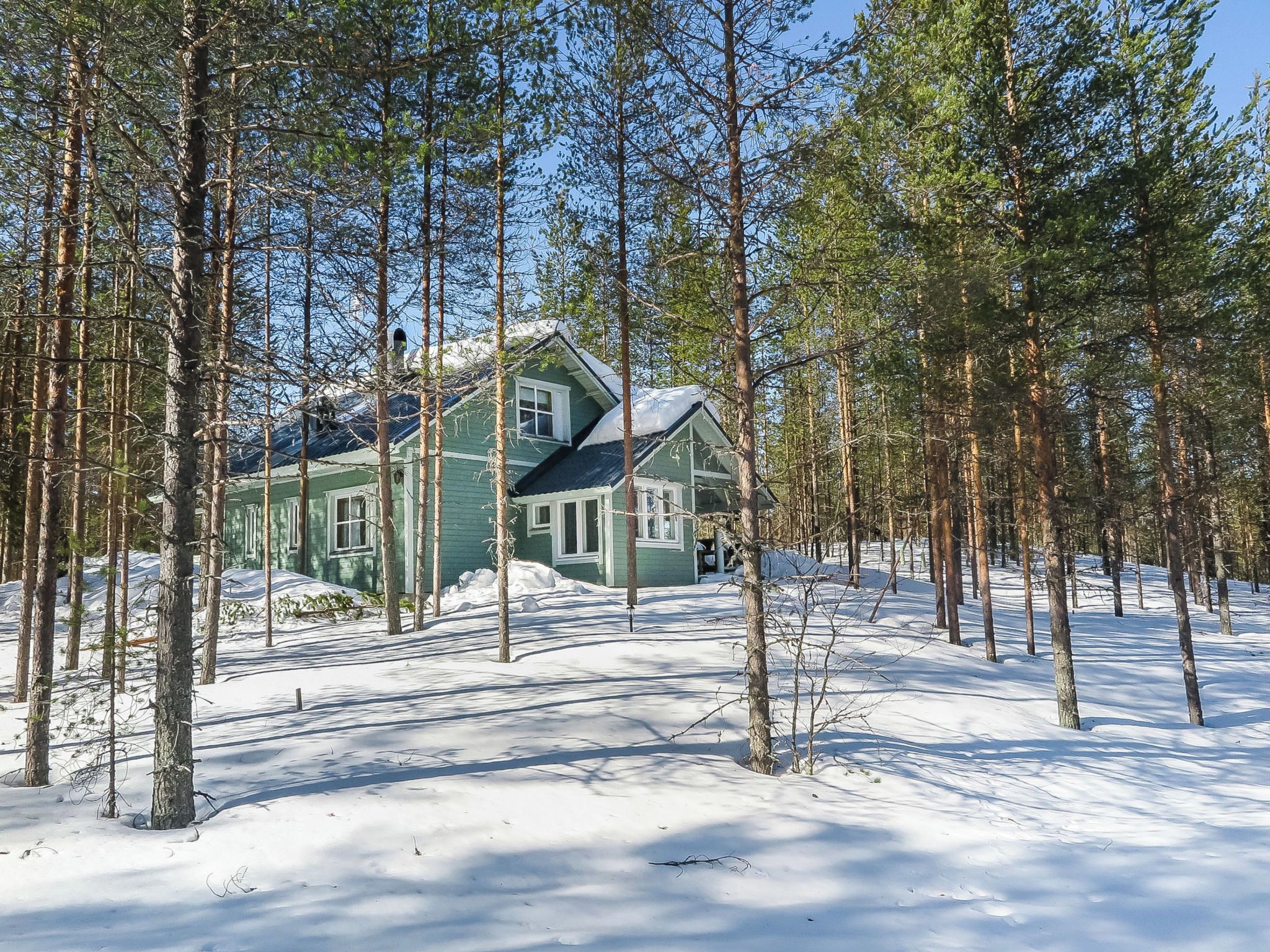 Een huis met twee verdiepingen, omringd door een bos, met sneeuw op de grond.