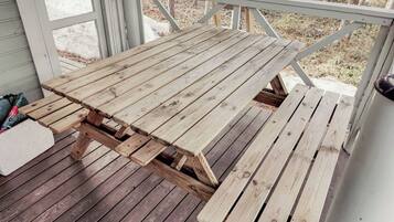 Een houten picknicktafel op een veranda met uitzicht op bomen en een gazon.