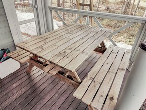Una mesa de picnic de madera en un porche con vistas a árboles y una zona verde.