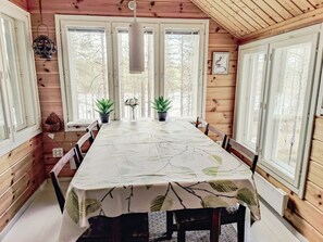 Una cabaña de madera con una mesa de comedor, sillas, plantas en macetas y vistas a árboles a través de amplios ventanales.