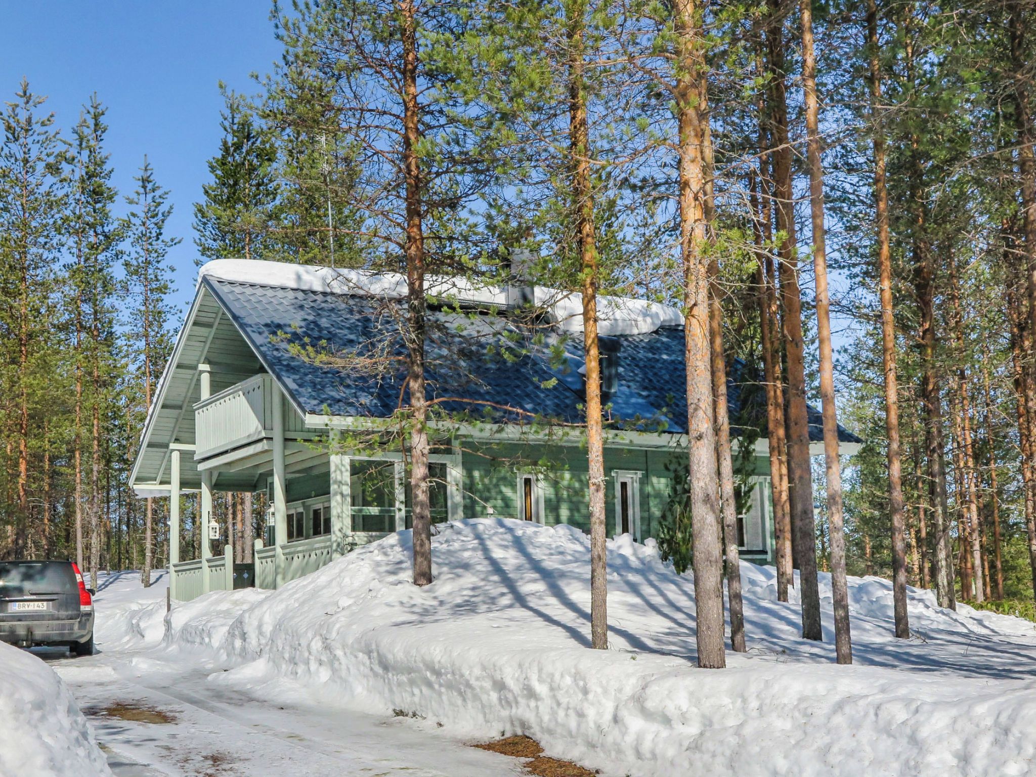 A cabin with a sloped roof, surrounded by a forest and covered in snow.
