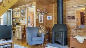 A cozy cabin interior with a fireplace, wooden walls, a comfortable chair, and a television.