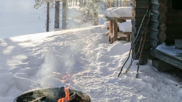 A snow-covered outdoor area with a fire pit, wooden benches, and a cabin.