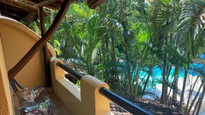 Un balcón con una mesa y sillas de vidrio, con vista a una piscina rodeada de vegetación exuberante.