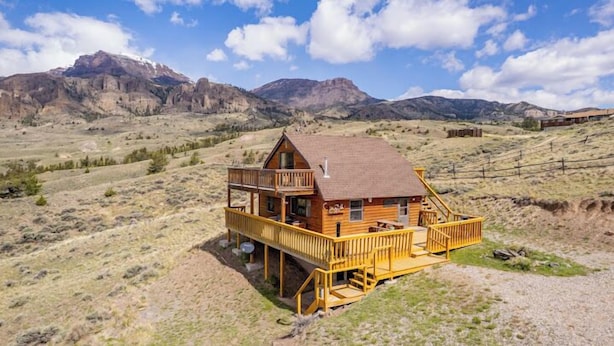 Een houten chalet met balkon, omgeven door een bergachtig landschap.