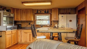 Een compacte keuken met houten kastjes, een ingebouwde oven, een koelkast en een raam dat voor natuurlijk licht zorgt.