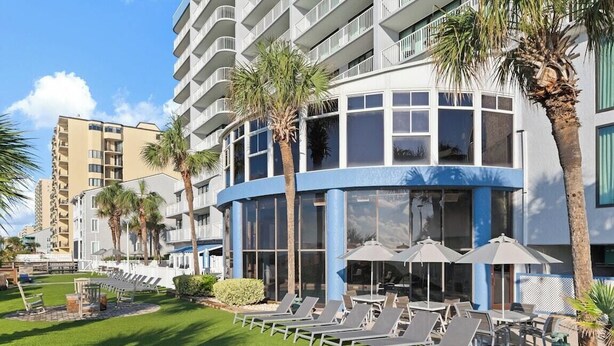Un hotel con zona de piscina, tumbonas y palmeras.