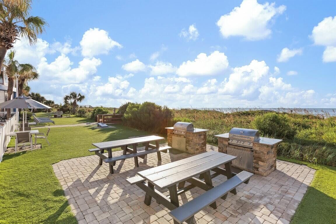 Une terrasse extérieure avec des tables de pique-nique et un espace barbecue, donnant sur une pelouse et un plan d’eau.