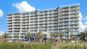 Un hotel de varios pisos con balcones, techo plano y ubicación frente a la playa.
