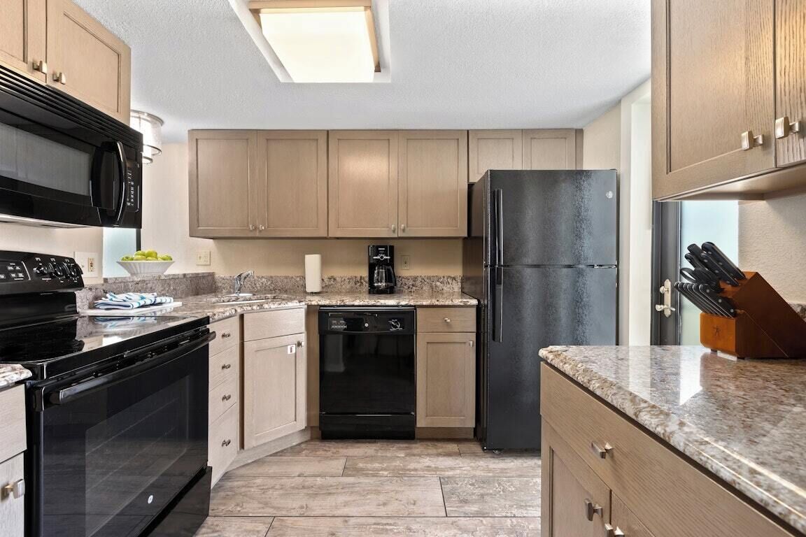 Eine Küche mit Holzschränken, einem schwarzen Kühlschrank, einer Mikrowelle, einem Backofen und einem Geschirrspüler.
