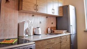 A modern kitchen with wooden cabinets, a stainless steel refrigerator, a stove, and a sink.