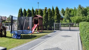 A playground with a trampoline, slide, and climbing structure, surrounded by a fence and trees.