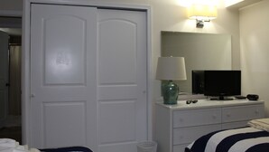 A hotel room with a white wardrobe, a bedside table with a lamp, a television, and a bed with striped bedding.