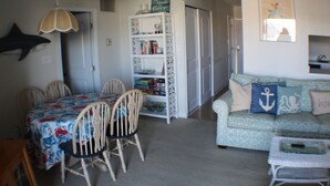 A dining area with a table and chairs, a bookshelf, a sofa, and a small table with a tray.