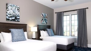 A hotel room with two beds, a large window with curtains, and artwork on the walls.