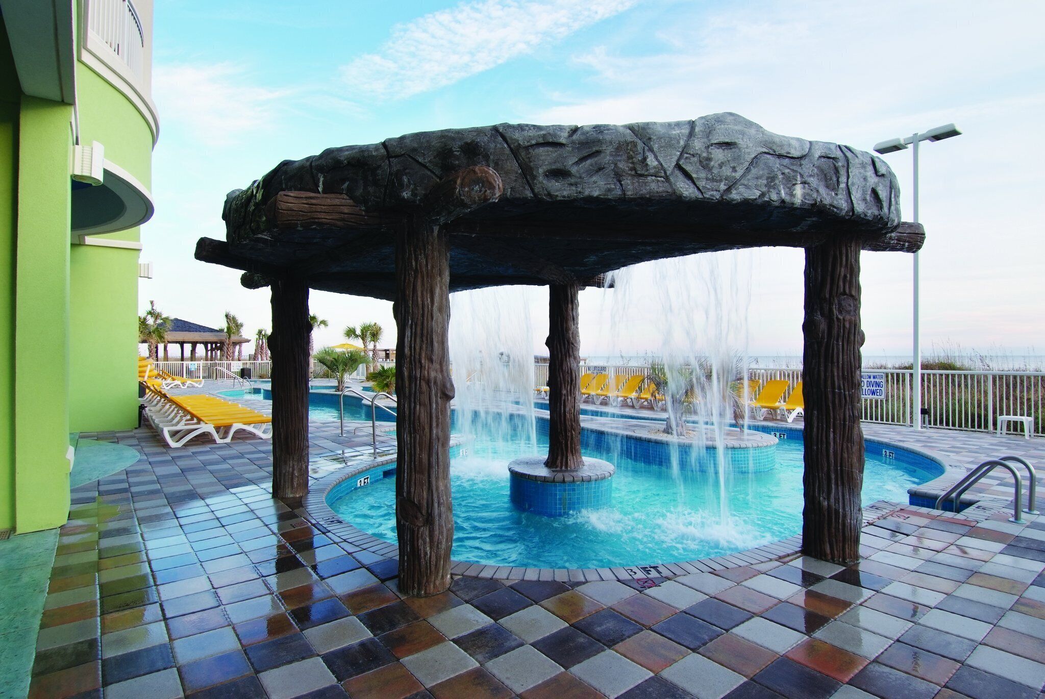 Un espace piscine agrémenté d’une structure en pierre, de jets d’eau et d’un sol carrelé.
