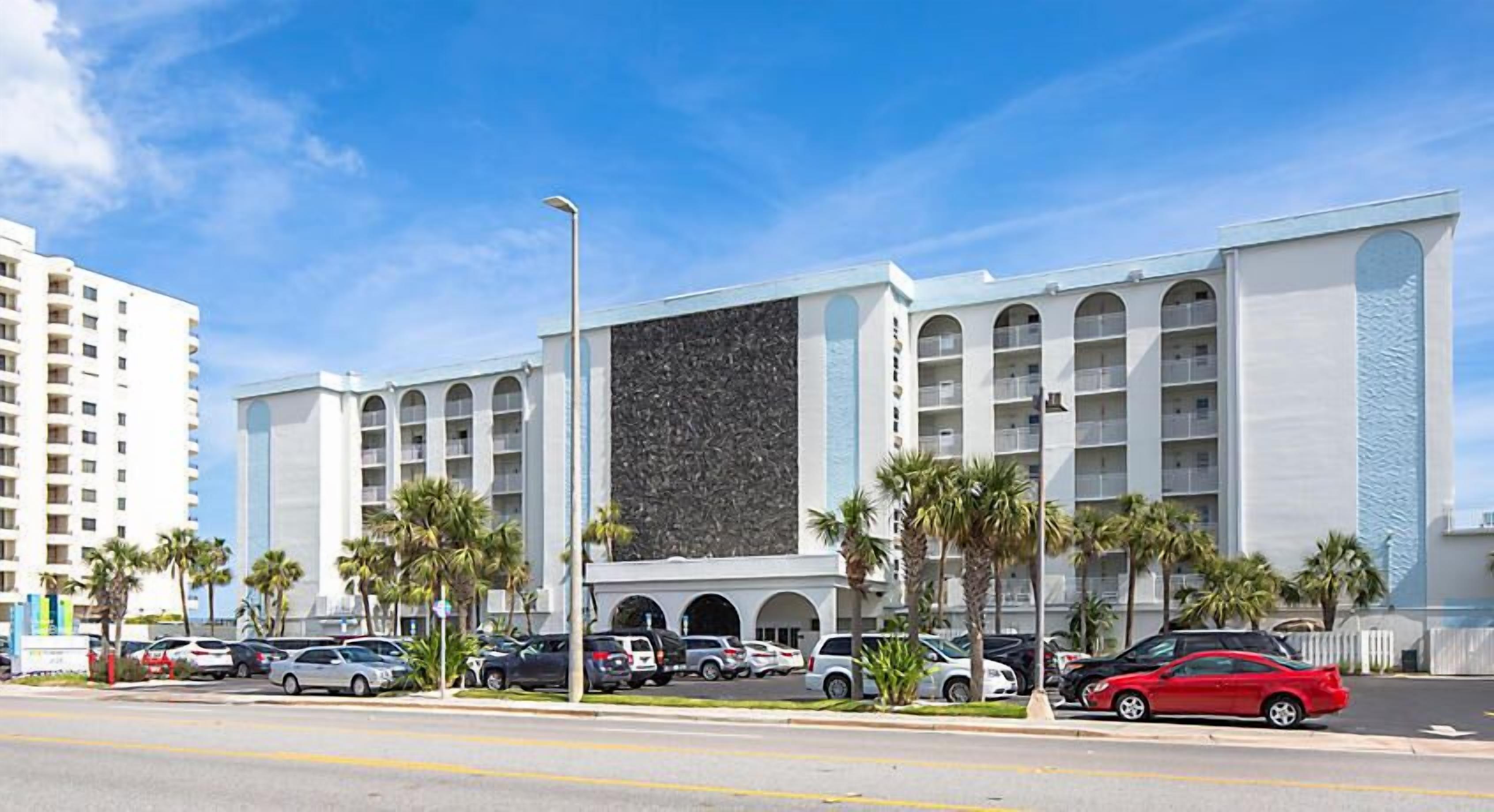 Un hotel de varios pisos, una amplia pared central y un estacionamiento con varios automóviles.
