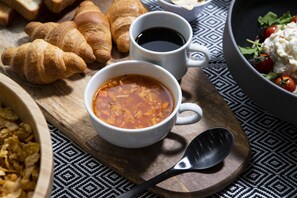 Une table dressée pour le petit-déjeuner avec des croissants, du café, une soupe et un saladier, le tout disposé sur une planche en bois.