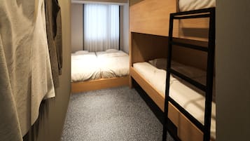 Een kleine hotelkamer met een stapelbed, een klein raam met gordijnen, een wandairconditioner en een kast met daarin hangende kleding.