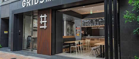 A modern hotel with a prominent sign reading "GRIDS HOTEL + HOSTEL". Inside, there are wooden tables and chairs, a chalkboard menu, and a seating area with a high ceiling.