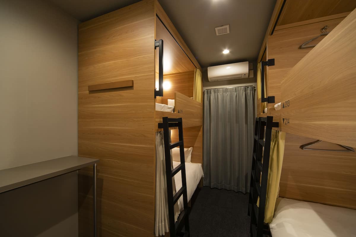 Una habitación de hotel compacta con literas, un escritorio pequeño y una ventana con cortinas.