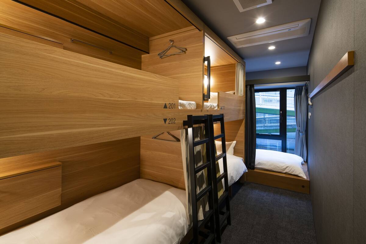 Habitación de hotel pequeña con literas, un escritorio y ventana con vista al exterior.